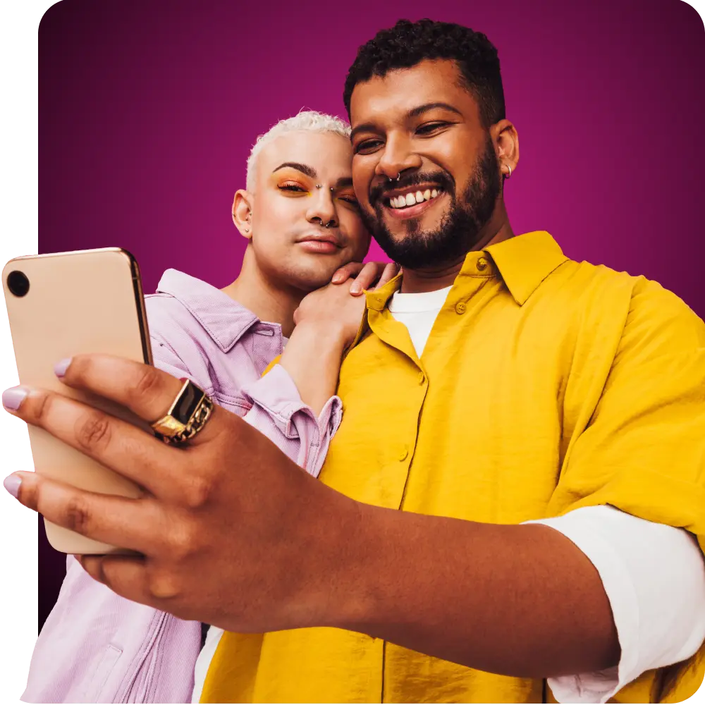 A gay couple in bright clothing smiling while looking at their phone